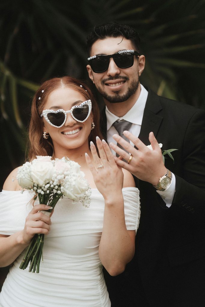 Vanessa and Bryant showing their wedding rings in playful sunglasses