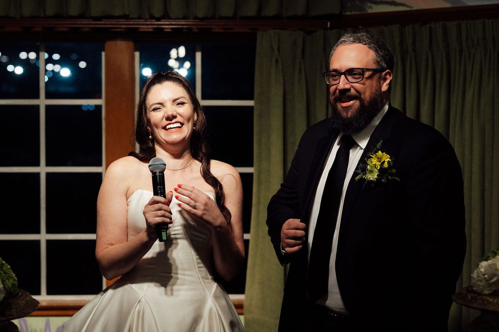 Catie and Tracy smiling during a wedding reception toast